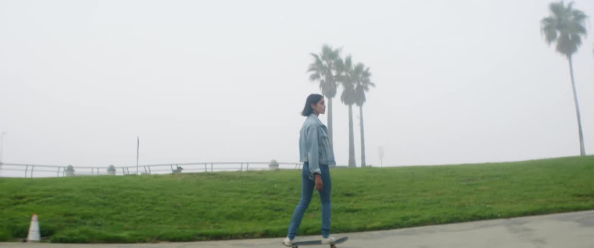 A young woman rides a skateboard in a quiet public park area