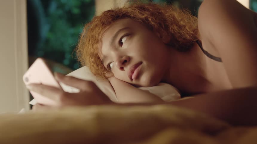 A black woman lies on a bed with her smartphone in her hand