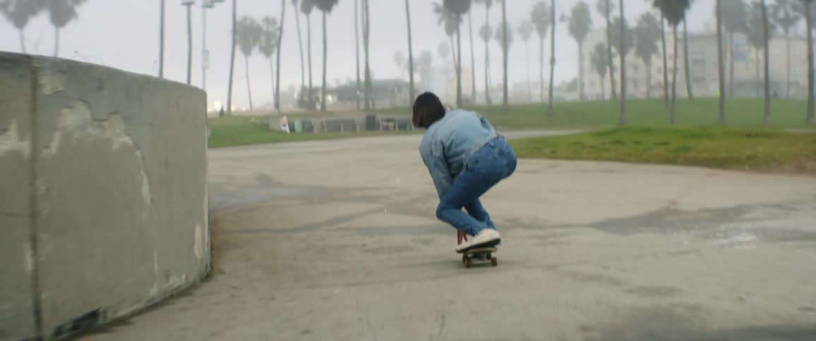 A teenager dressed all in denim rides a skateboard through a public park
