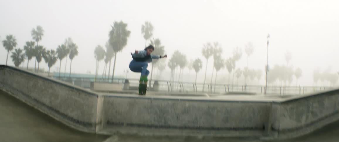Woman rides skateboard in a jump in foggy park