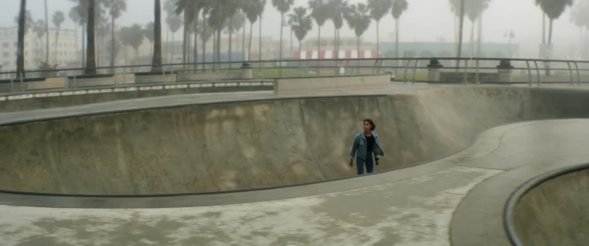 A teenage girl rides a skateboard in a park and performs a jump