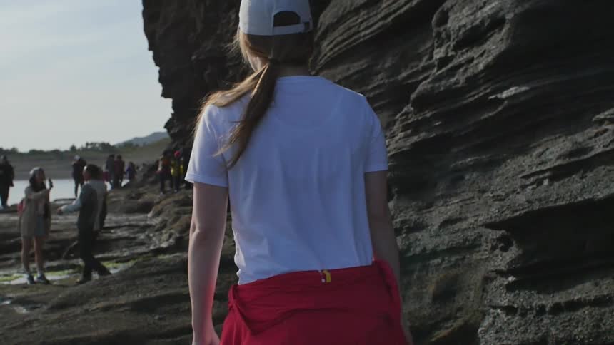 A woman walking toward a group of people near a cliff on a beach