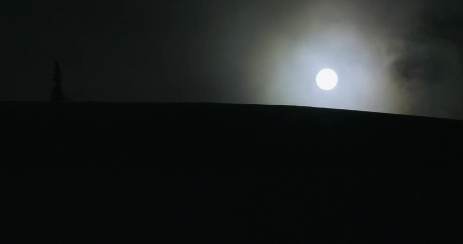 The full moon looming over a hill cloaked in darkness