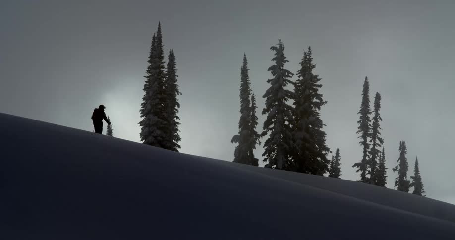 A silhouette of a person on skis walks across the top of a hill