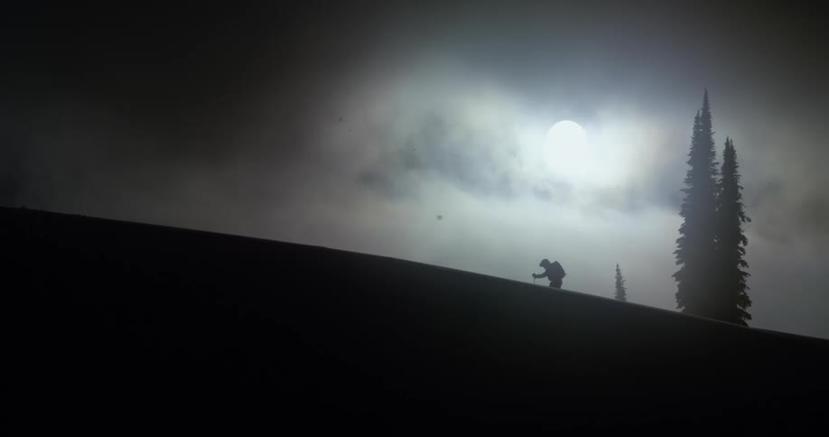 A skier hikes up a mountain backlit by the sun