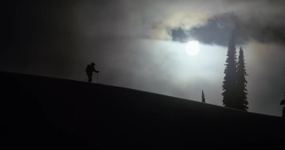 A hiker walks across a mountain silhouetted by the sun