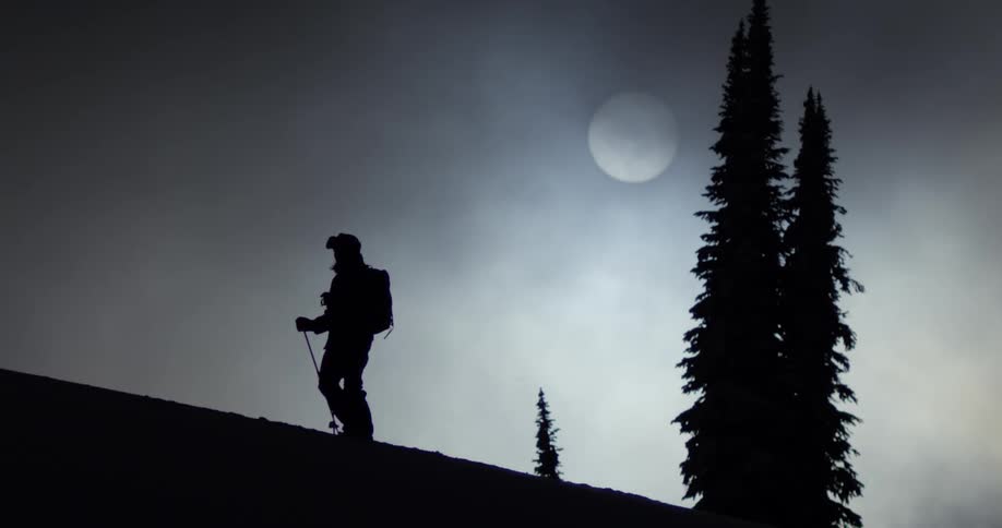 A skier walks up a hill in silhouette