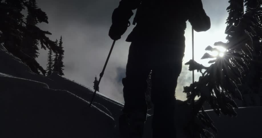 A silhouette of a person hiking in snow with the sky and trees in the background