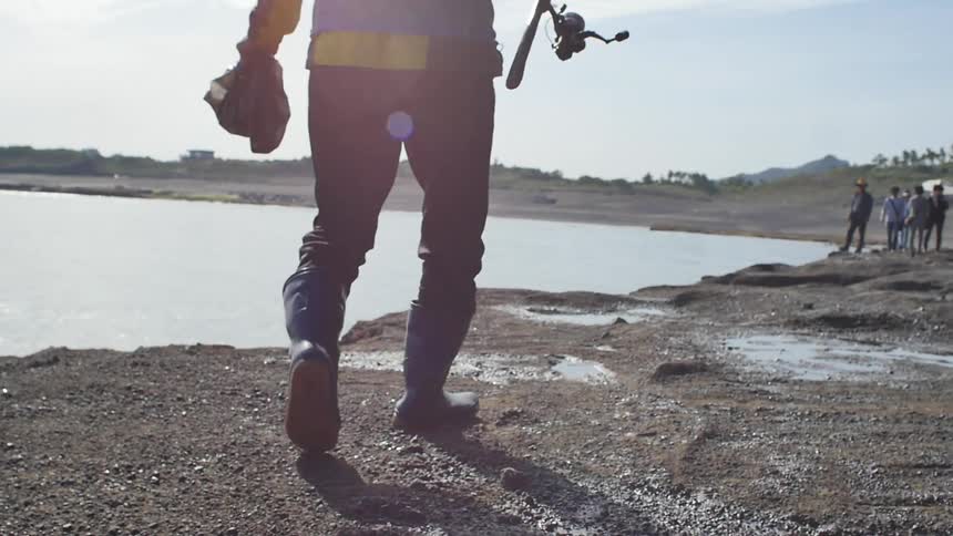 A man carrying fishing gear walks along a shoreline