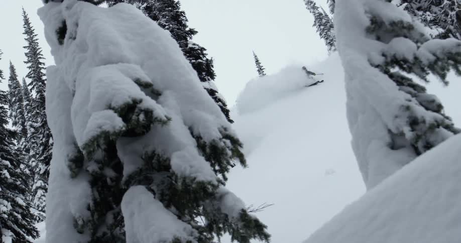 A skier kicks up a cloud of snow skiing down a mountain slope