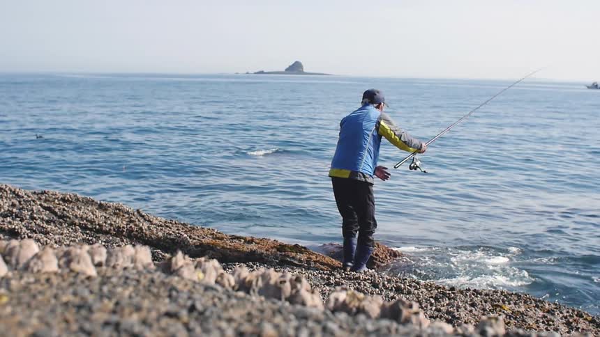 A man in blue fishes from the ocean