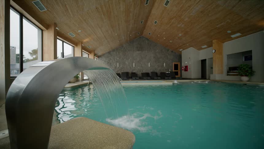 An indoor pool features a waterfall and floor to ceiling windows