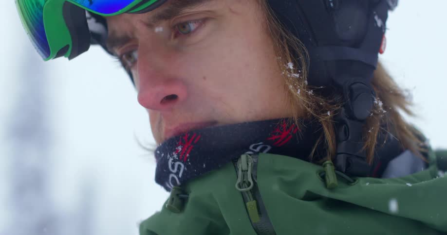 A man wears ski goggles and a coat while standing outside in the snow