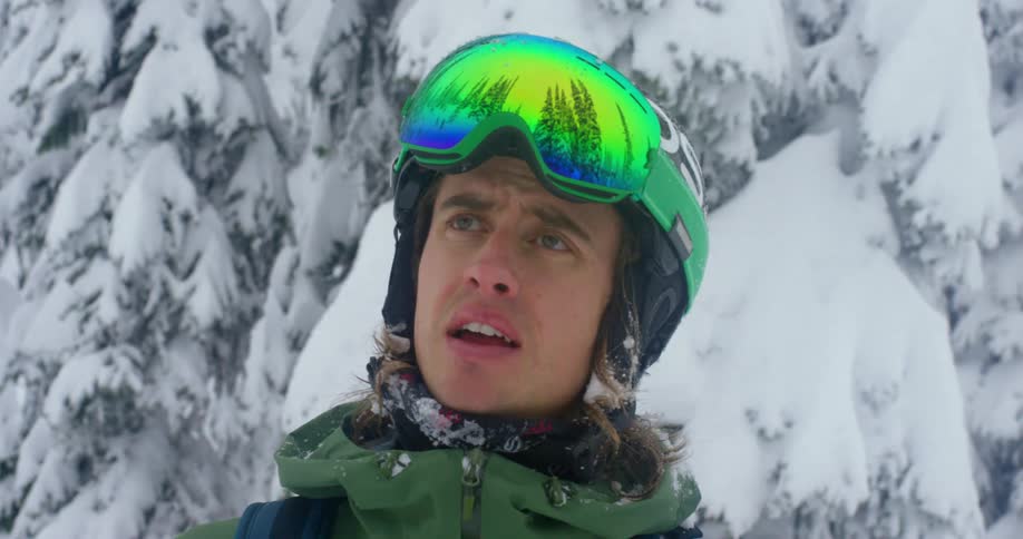 A man wearing ski goggles stands in front of trees covered in snow