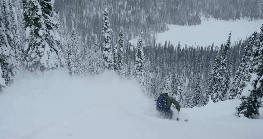 A person skis down a snow covered mountain surrounded by trees