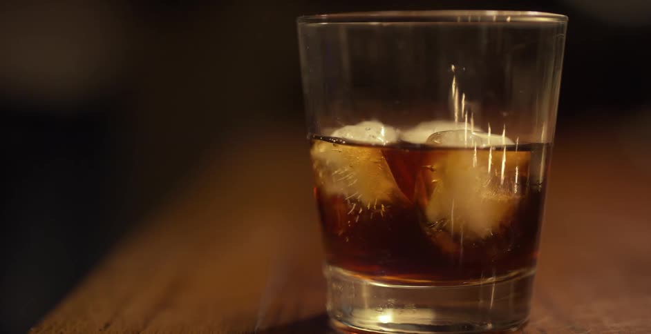 A bartender slides an iced drink across the bar to the camera