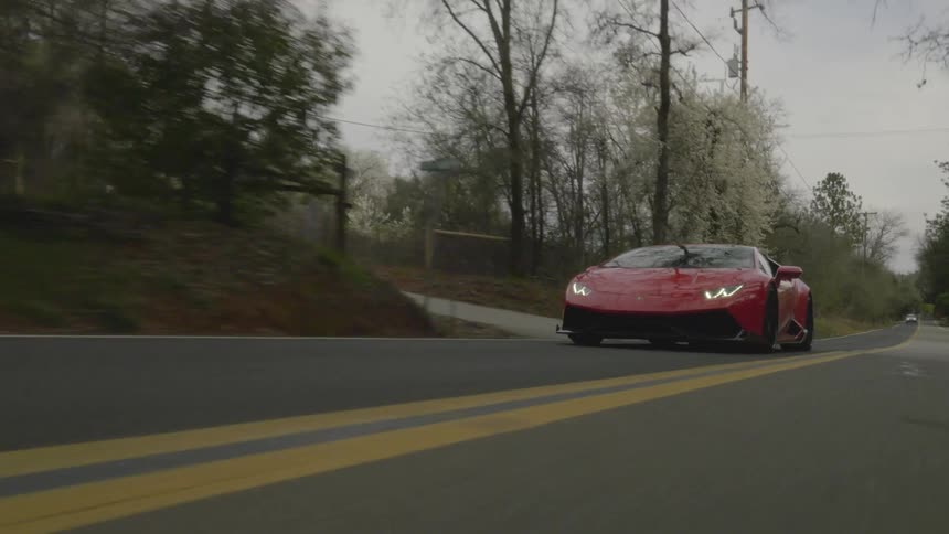 A red car drives down the road on a cloudy day