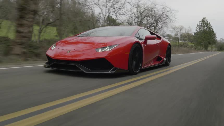 A red sports car driving fast on a two lane road