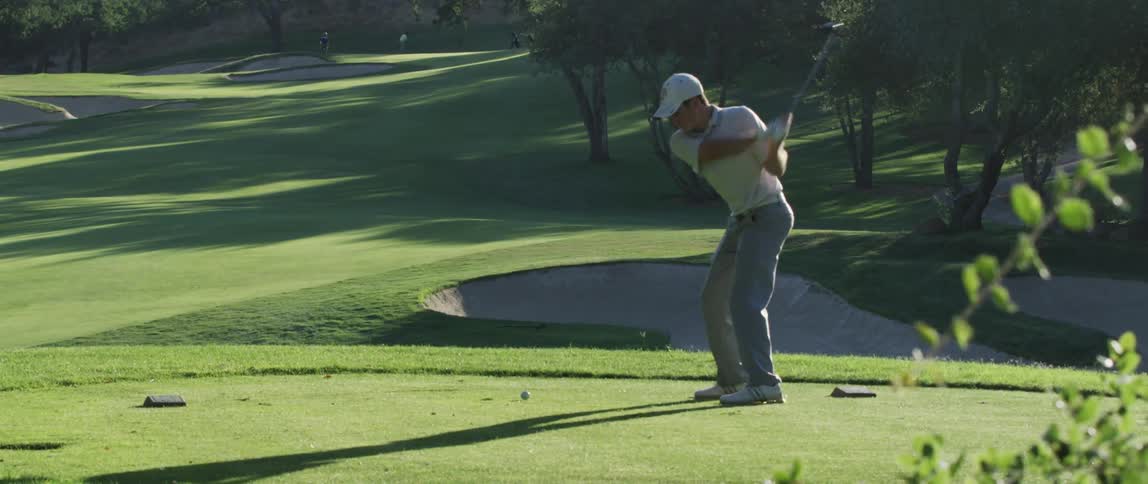 A man drives a golf ball on a sunny day