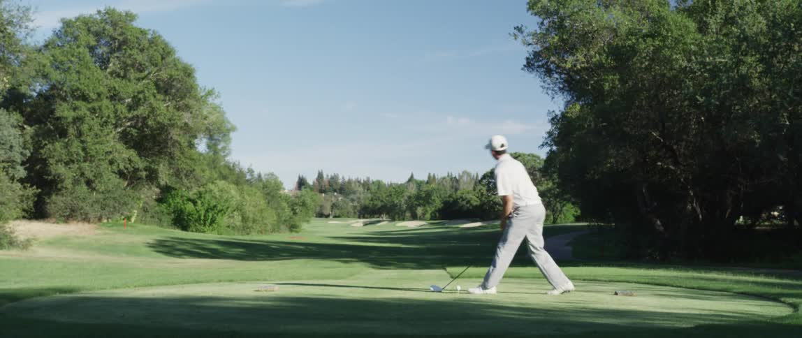 Man puts a golf ball onto a tee and swings his club