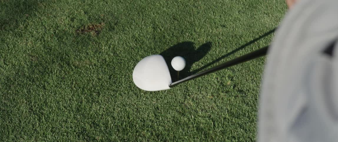 A golf club is lined up with a ball on the grass