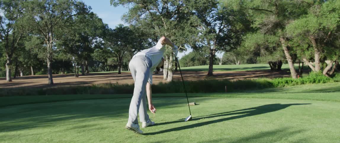 A young man places a tee on a golf course