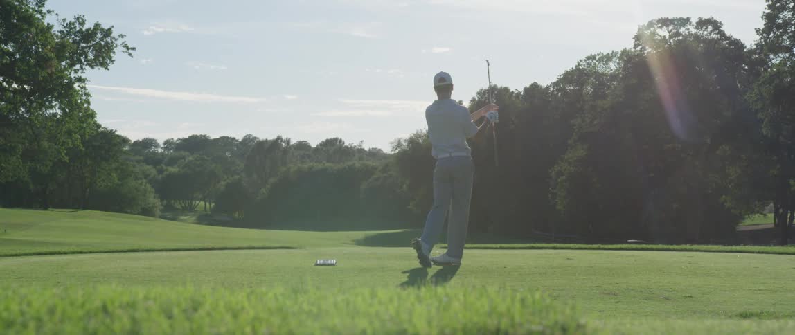 A man drives a golf ball down a course on a sunny day