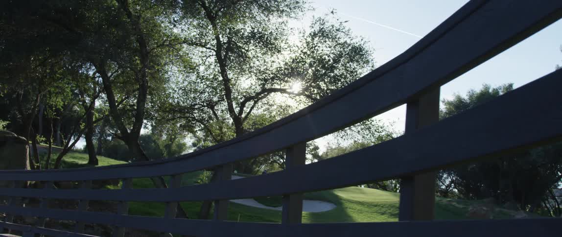 Slow moving across a bridge showing a field past a railing
