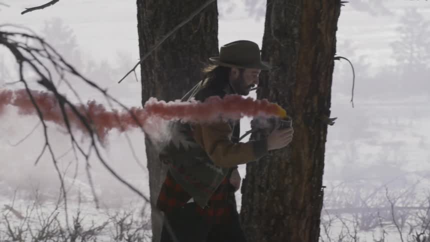 A man is running through a snow covered area with a can giving off red smoke
