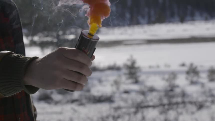 A person holds a flare while it releases multi-colored smoke in slow motion