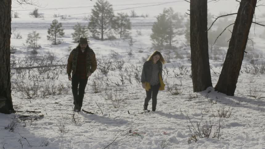 A man and woman are walking across a snow covered field