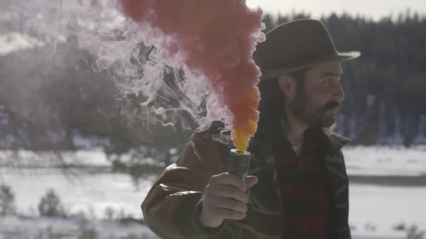 A man holds a red smoke bomb and looks around