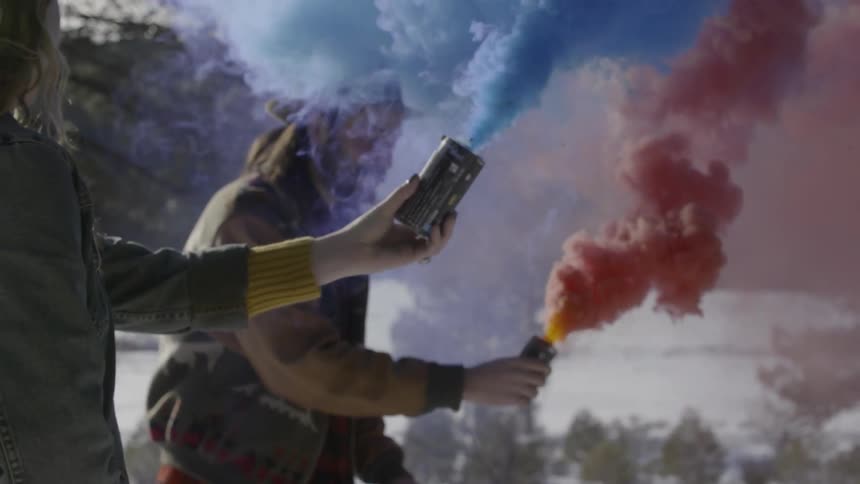Two people hold smoke canisters that are emitting colorful smoke