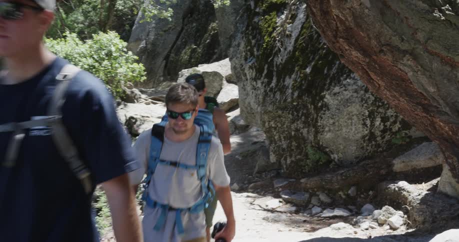 Three people are hiking along a cliff on a sunny day
