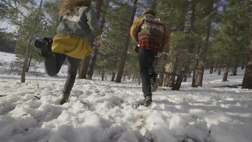 A man and woman running through the snow in a sparse forest