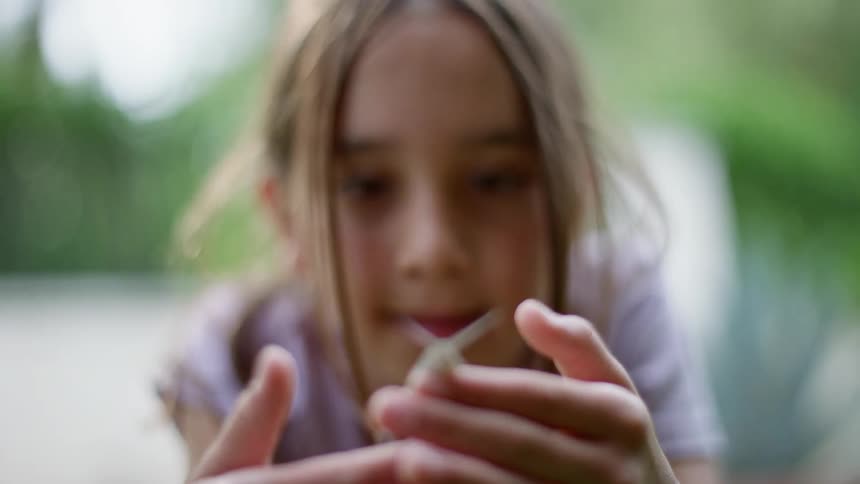 Girl with unkempt hair holds and studies snail outdoors