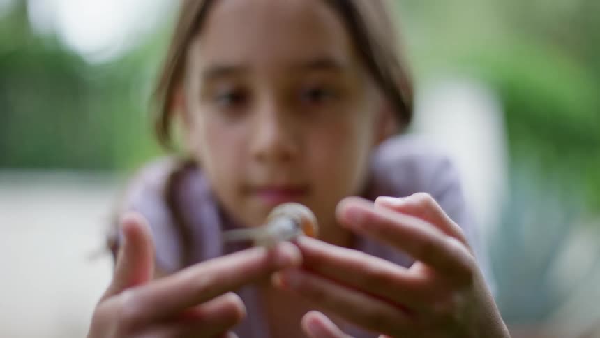 Girl holds touches and studies snail outdoors