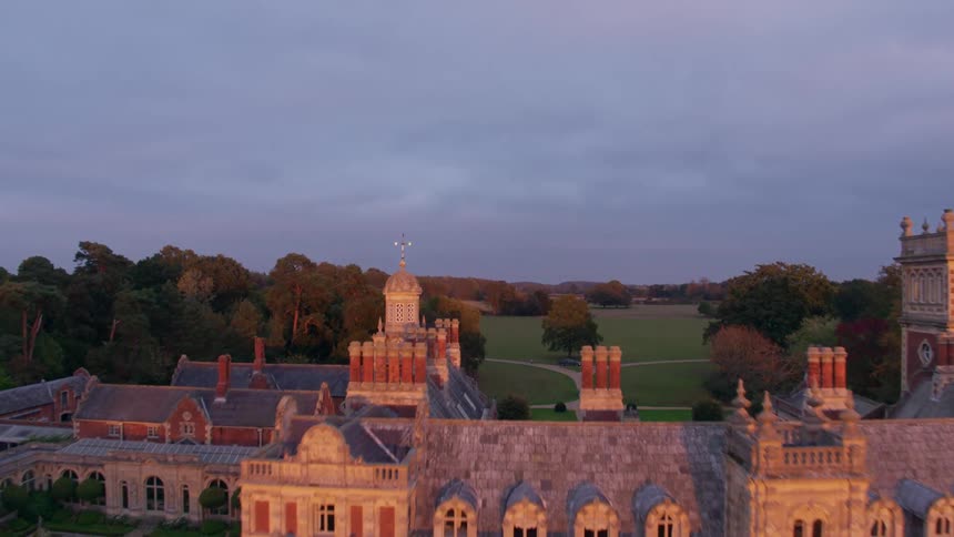 Sun shines on ornate mansion and garden surrounded by forest and fields