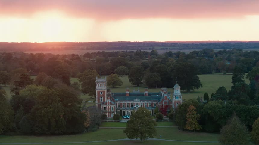 A large manor in a rural wooded landscape under a low sun
