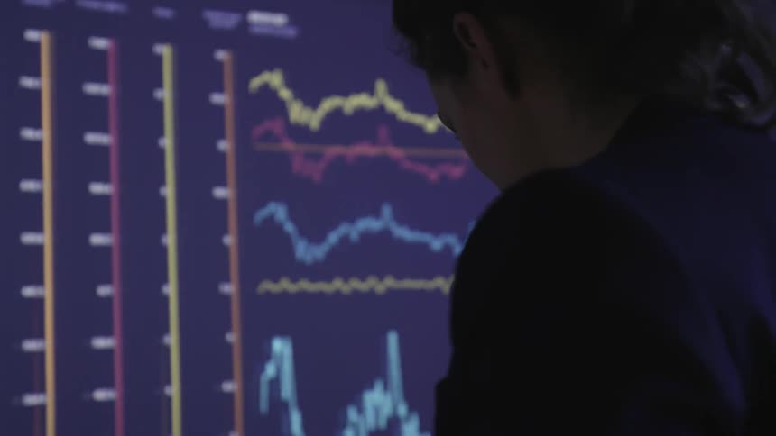 A woman in an office with graphs on a large screen in front of her