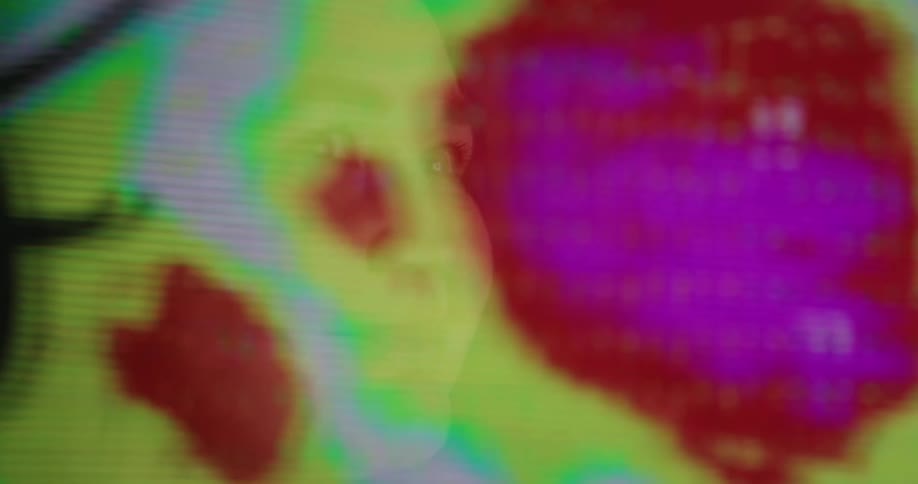 A white womans face is reflected in a monitor showing weather patterns forming
