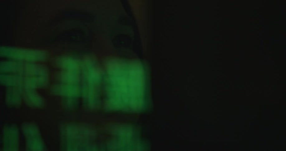 A white woman sits and smiles as computer text is reflected off of her face