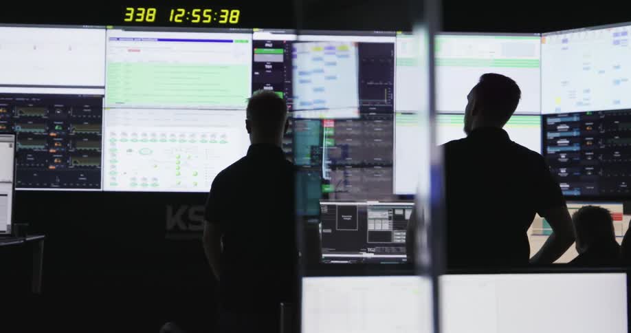 Group of men working on a control room lined with multiple lcd screens