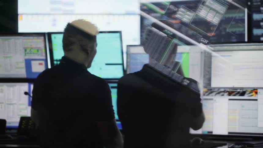 Two men stand in room full of monitors and displays talking and reviewing data