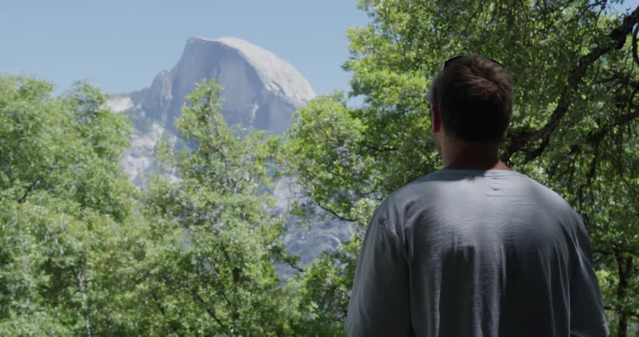 A man is walking outside in the wilderness and looks towards a mountain