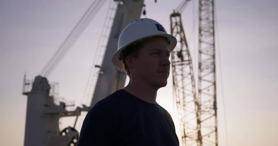 Man wearing a hard hat stands near cranes on construction site at sunset