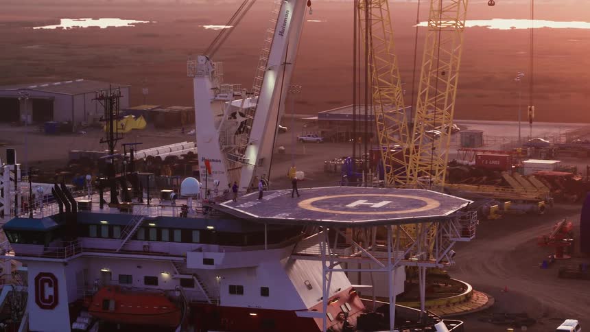 People walk in a helicopter landing pad attached to a boat while scaffolding stands nearby
