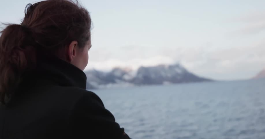 Woman wearing a coat watches the ocean from a boat