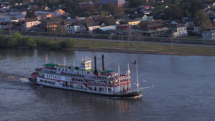 A riverboat traveling down a river next to the residential area of a city