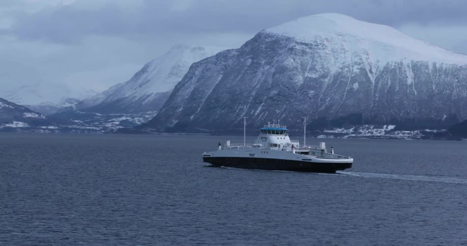 Ferry boat travels across the sea with the snow capped mountains in the background